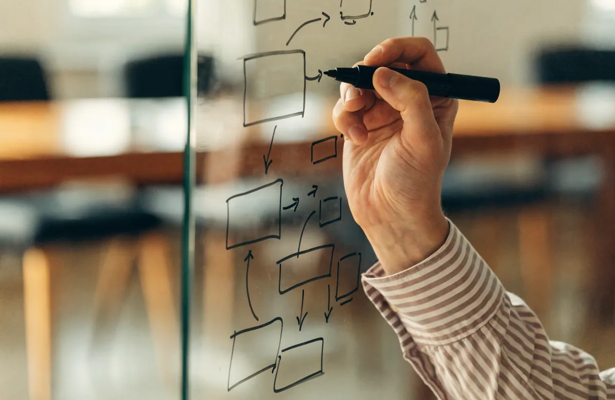 Main traçant un schéma sur un tableau vitré